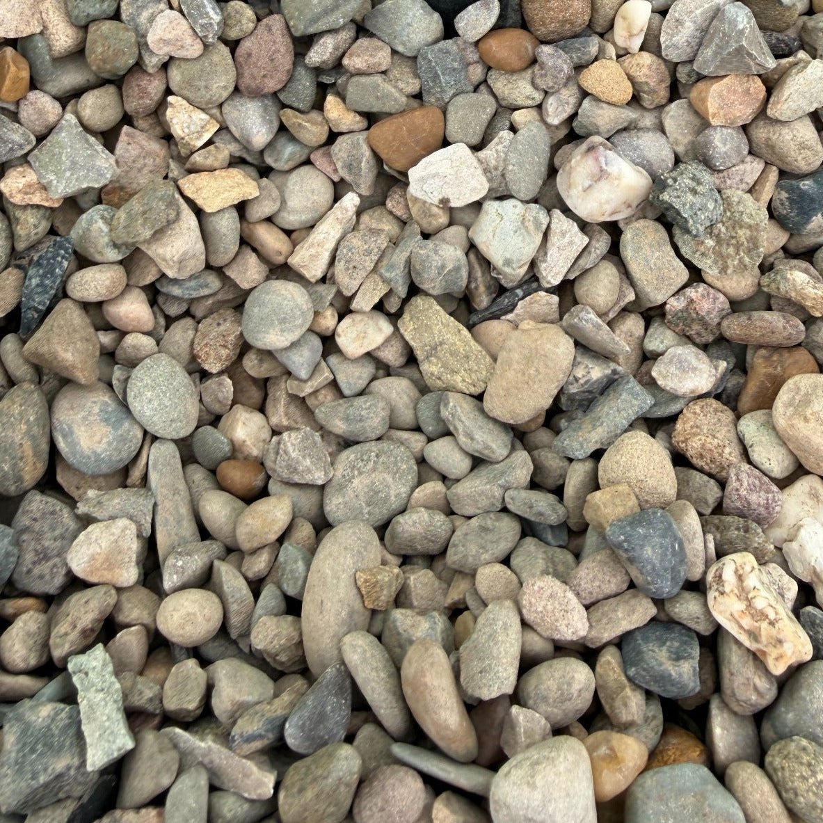 A close-up of small pebbles and gravel in a green container, with a small black handwritten label reading 'WELSH BROWN 10MM'.
