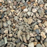 A close-up of small pebbles and gravel in a green container, with a small black handwritten label reading 'WELSH BROWN 10MM'.